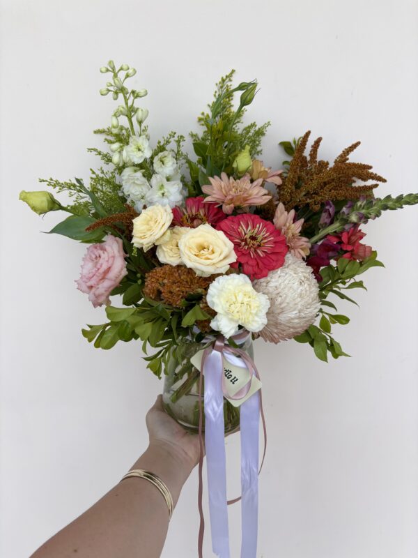 A hand holding a Small Vase filled with a mixed bouquet of pink, white, yellow, and red flowers