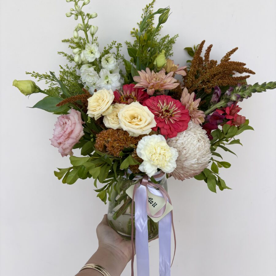 A hand holding a Small Vase filled with a mixed bouquet of pink, white, yellow, and red flowers
