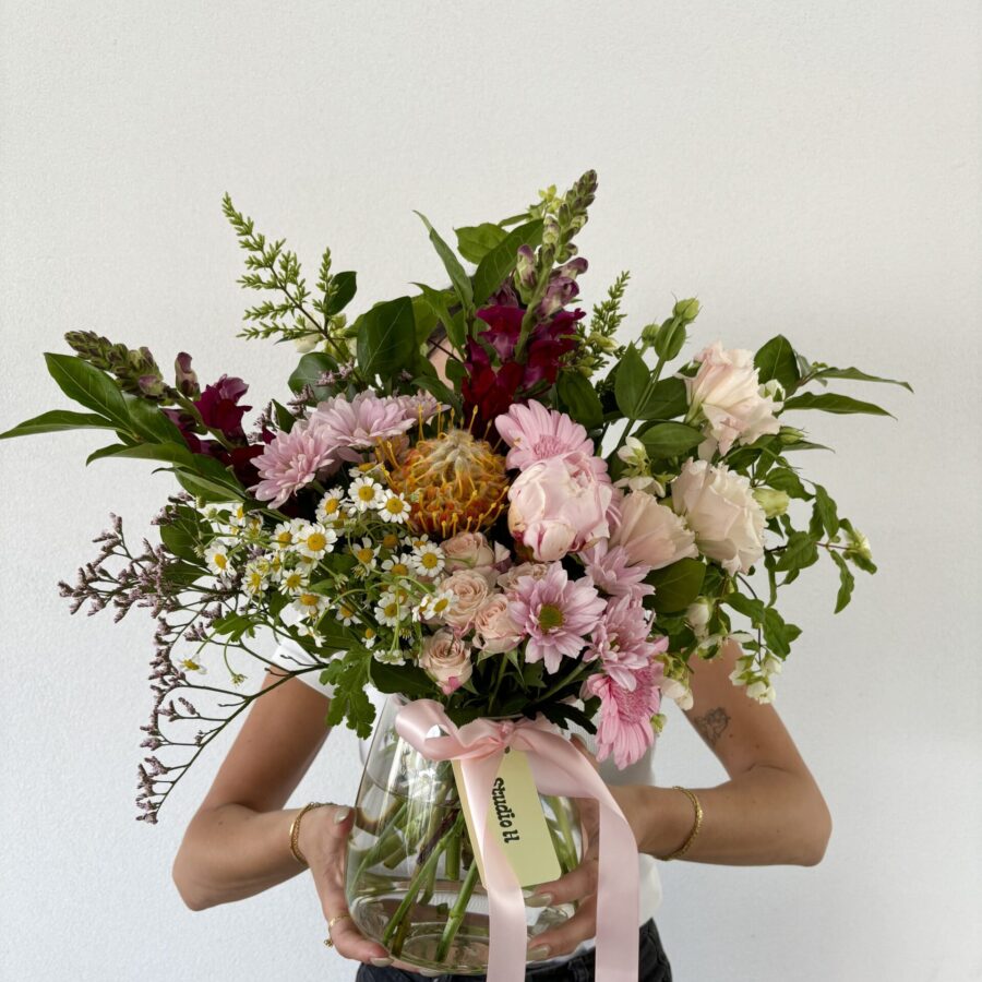 A person holds a large vase with a vibrant bouquet of pink gerberas and daisies.