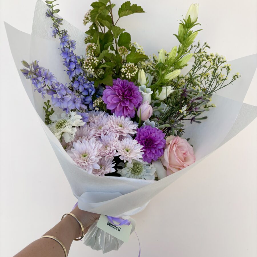 A hand holds a 'Small Bunch' bouquet with purple dahlias, pink roses, and greenery.